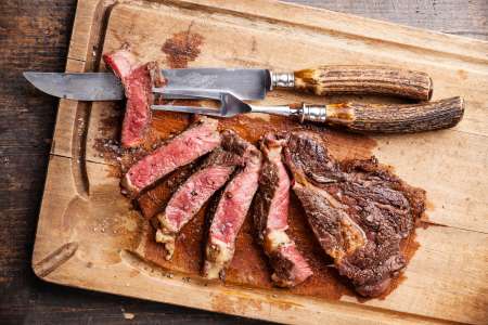 A steak sliced medium rare sits atop a cutting board.