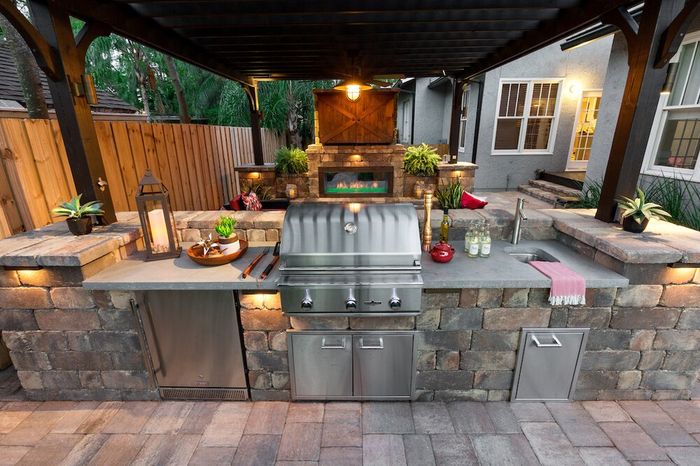 A stainless steel grill is sitting under a pergola in an outdoor kitchen.