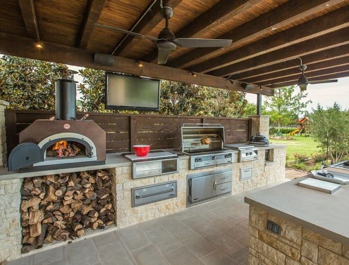 An outdoor kitchen with a pizza oven , grill , and television.