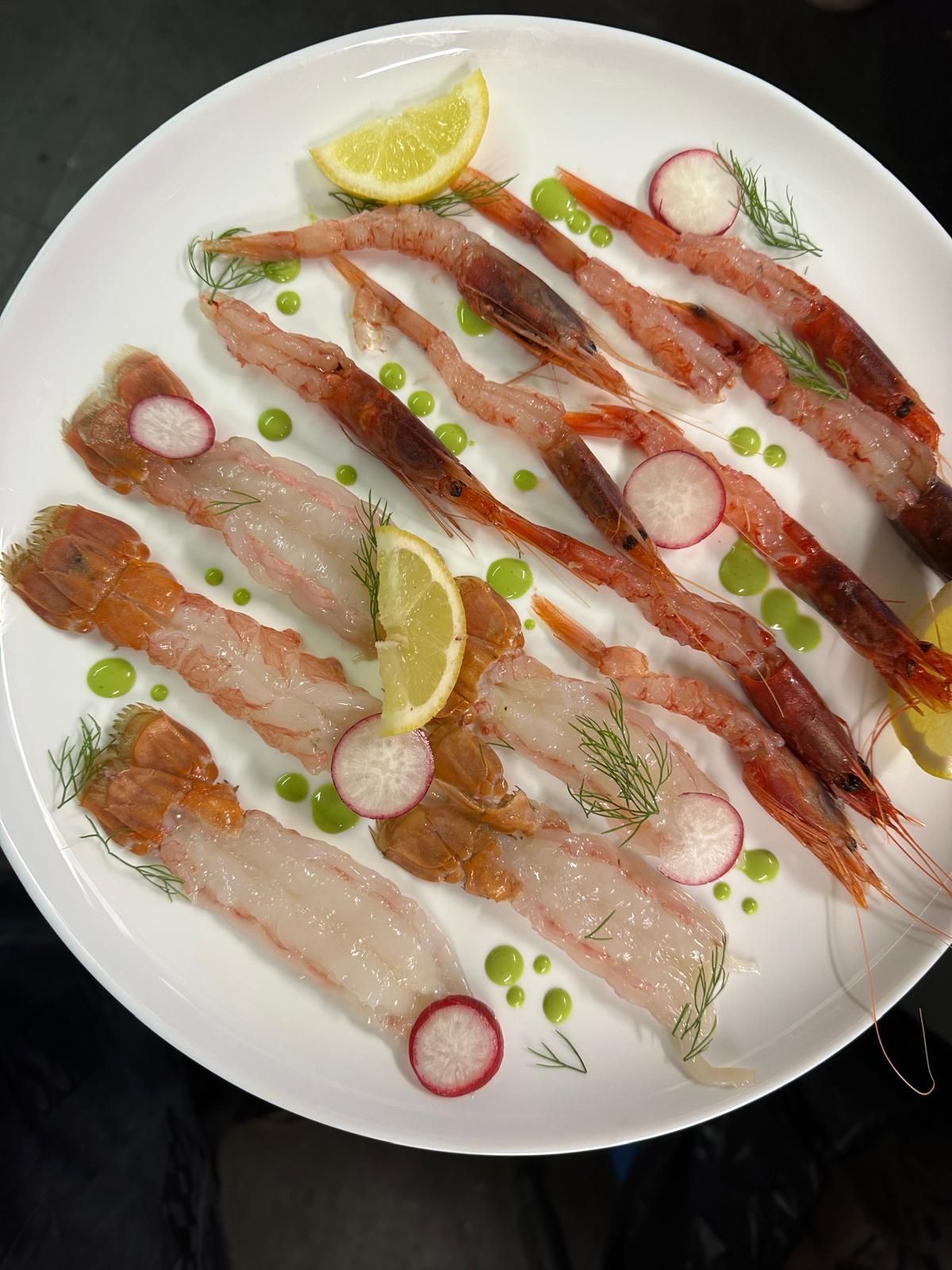 Piatto di sashimi di pesce crudo assortito con spicchi di limone, fette di ravanello e guarnizione verde su un piatto bianco