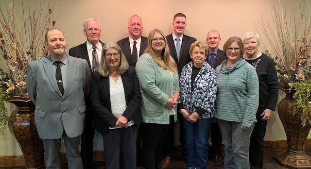 Group of people standing together indoors; several are wearing suits.