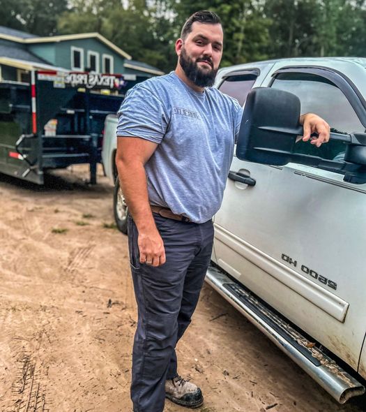 A man with a beard is standing next to a white truck.