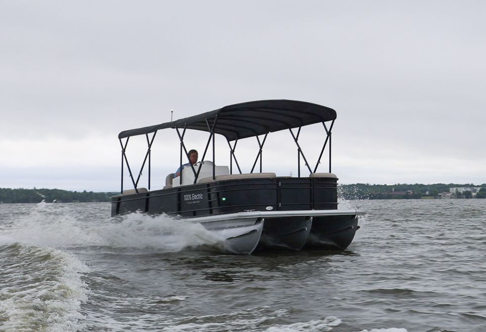 Black tritoon with bimini top up man sitting at helm driving boat producing small wake
