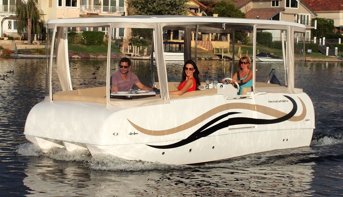 three people on a boat with a clear enclosure multihull cruiser with accents on the side. A woman is driving in the center console towards the back of the boat