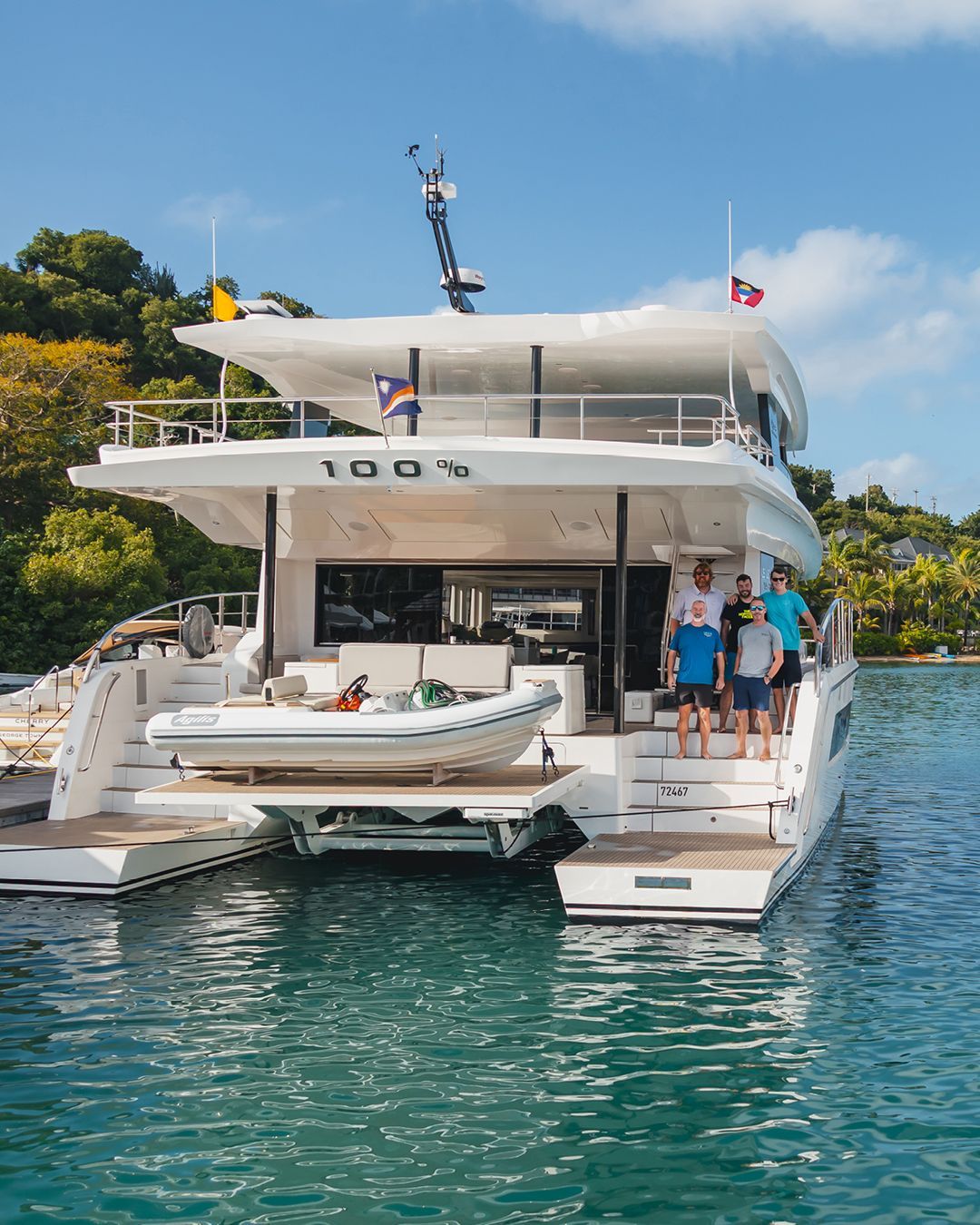 5 men standing on the steps of a multi story yacht with 100% engraved on the hulll of the yacht there is a RIB on the transom on a boat lift