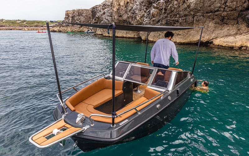 Man is standing at the back of a boat that has dolphin striker and canopy set up. Burnt orange interior seating and grey hull. 