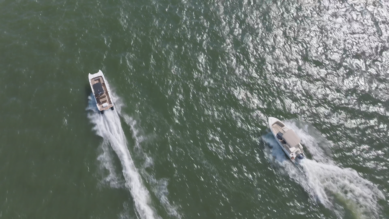 aerial shot of two boats moving fast in water. the boat on the left is a catamaran U shaped hull the boat on the right is a bowrider both have t tops and center consoles