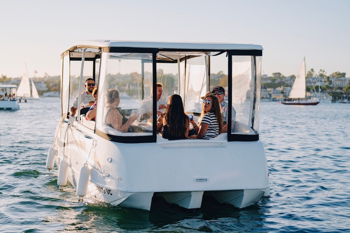 People on board electracraft 182TR having drinks and smiling boat on water sailboats in background