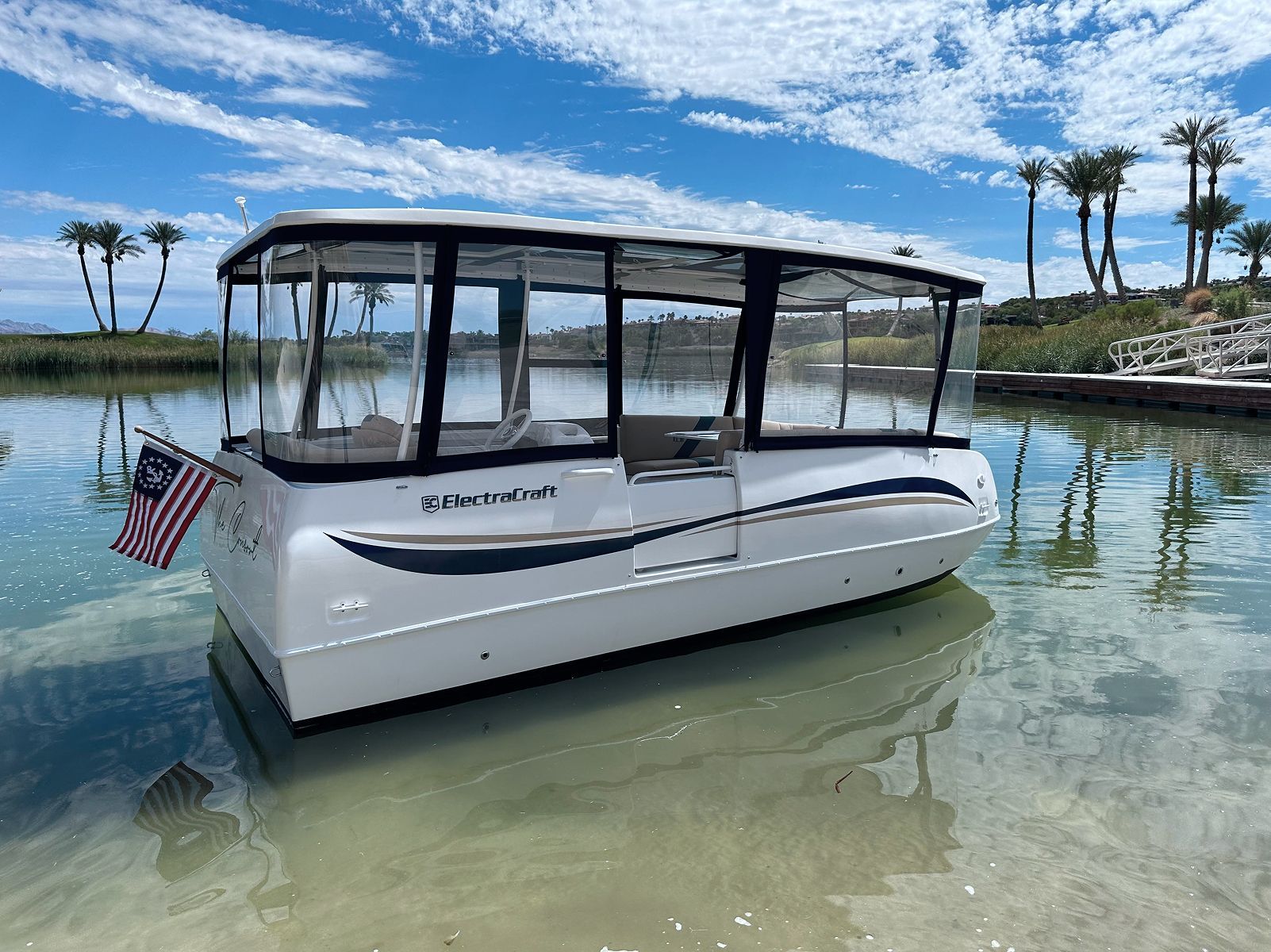 A white boat 16' ft is sitting in water with canopy installed and exclosures there is a blue stripe on the hull 