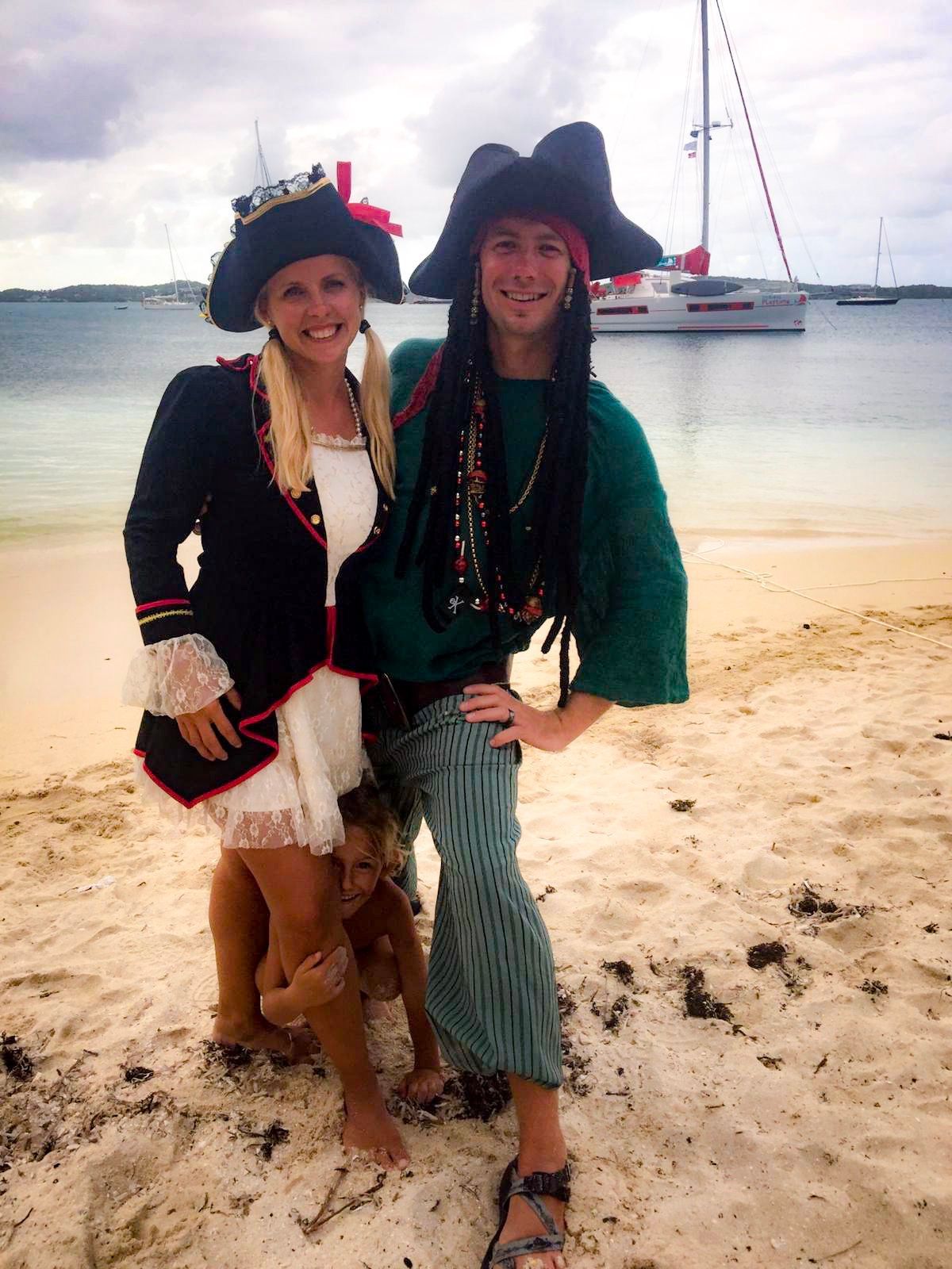 A man and a woman in pirate costumes are posing for a picture on the beach.