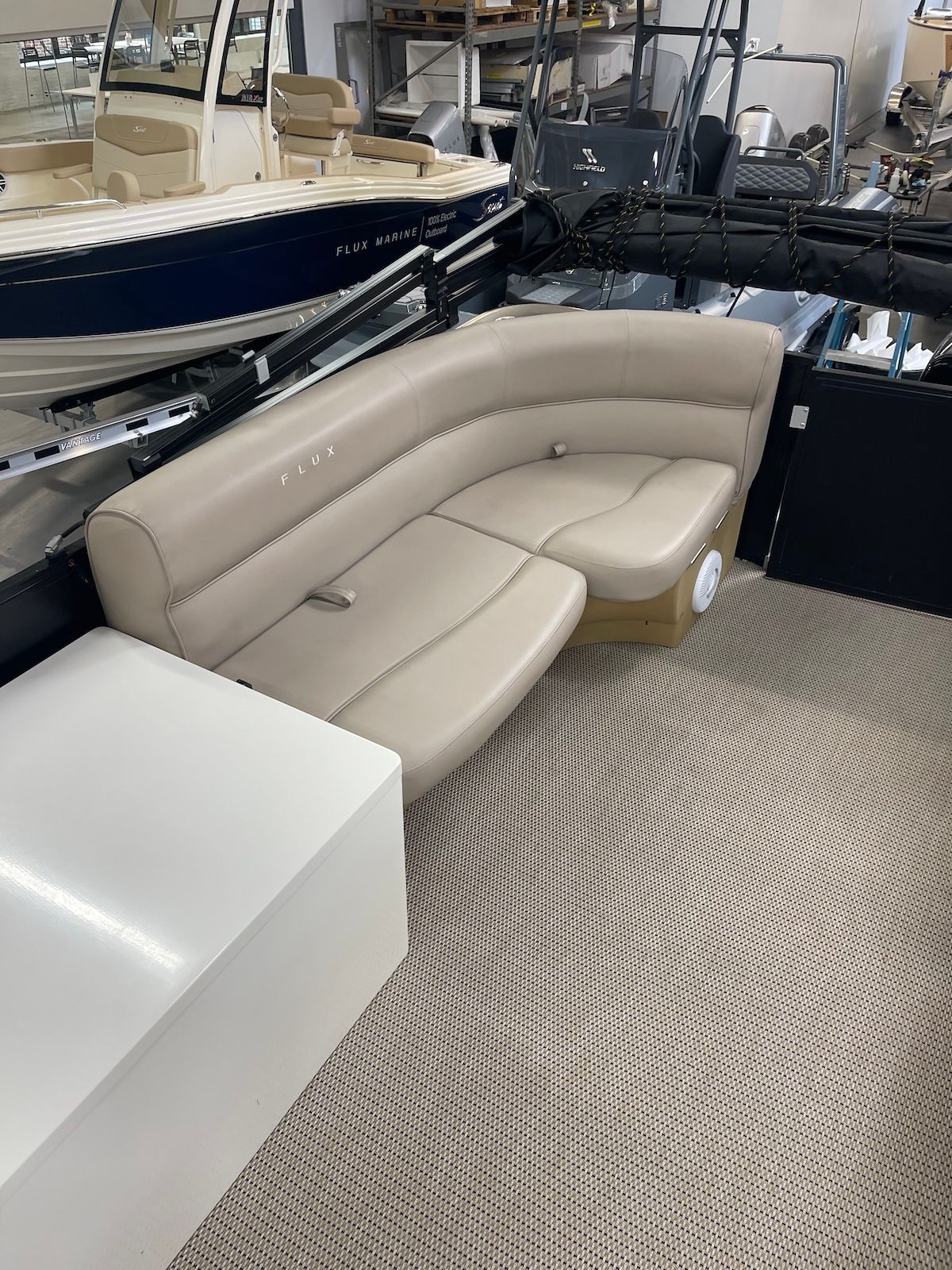 The left corner of a pontoon deck boat with beige interior showing seating and L shaped cushion