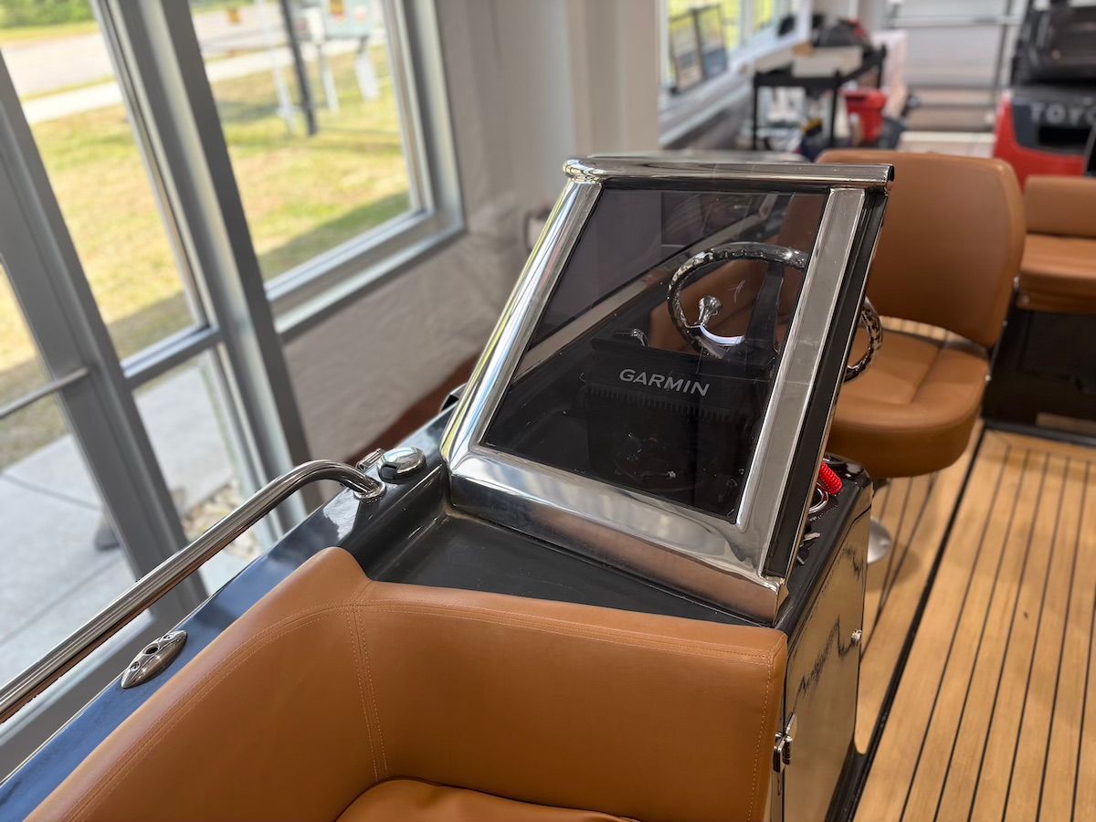 Looking at windshield on magonis with view of captain and helm station there is a window in the background showing grass area 