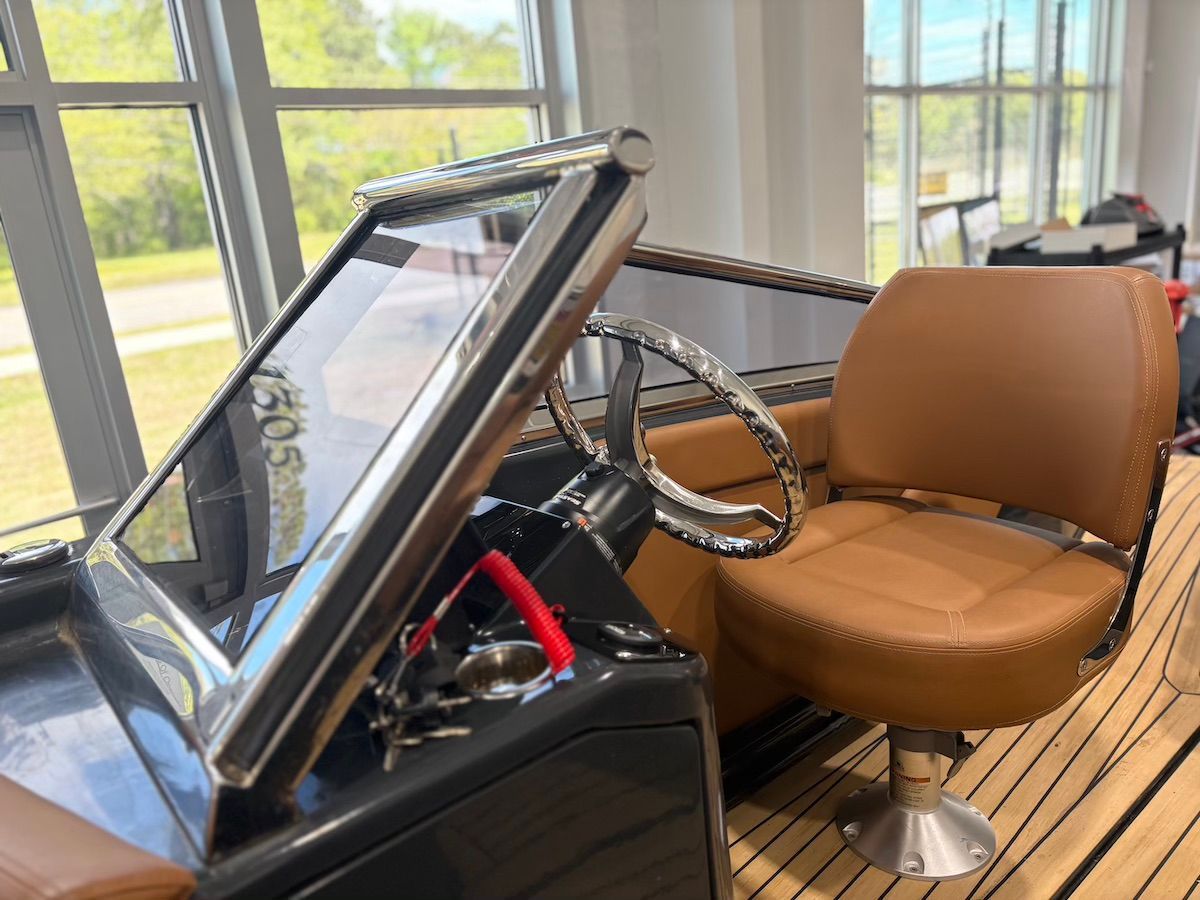 Captain seat on boat safety lanyard red still attached. There is a brown swivel captain chair with nice finished brown upholstery and brown teak flooring and stainless steel steering wheel