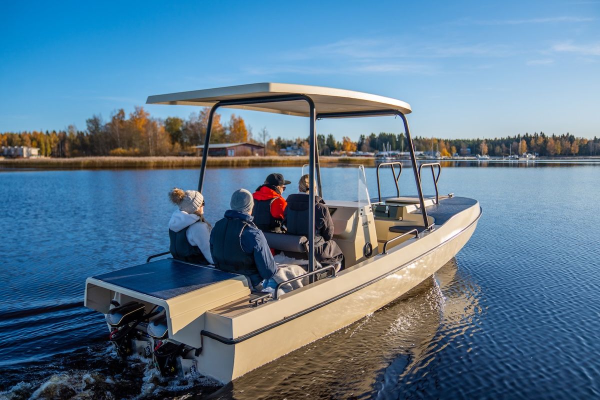 Four people on boat in winter attire. Fall foliage in background 