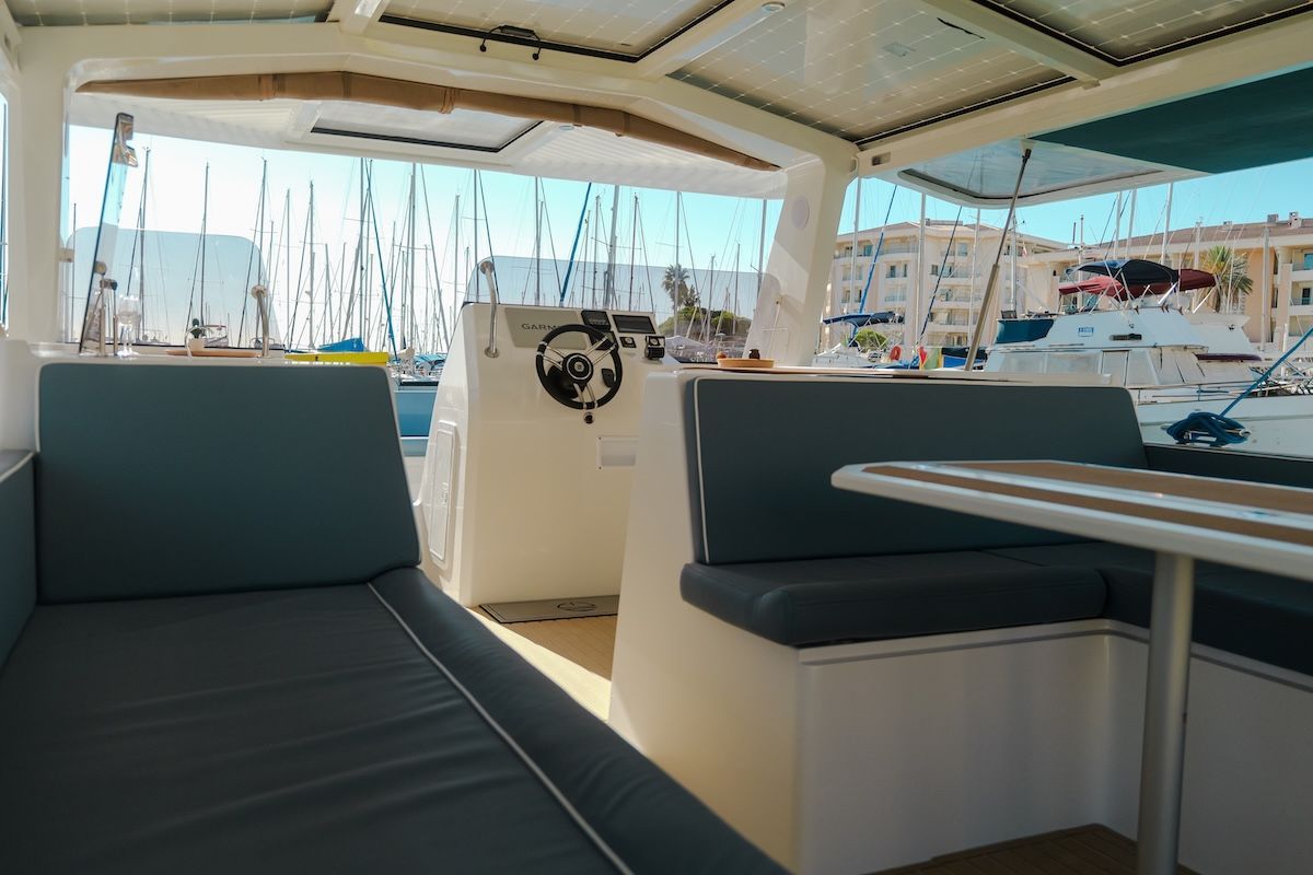 Alternative view of the captain helm station on a large boat with solar panel roof can see dining table and seat and layout and sailboats in background