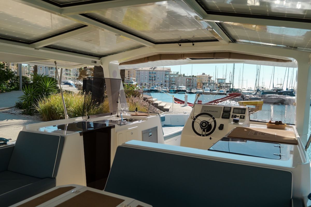 Overlook of helm station on a large boat white interior solar panel roof and blue cushions. picture is taken looking over bench in dining area