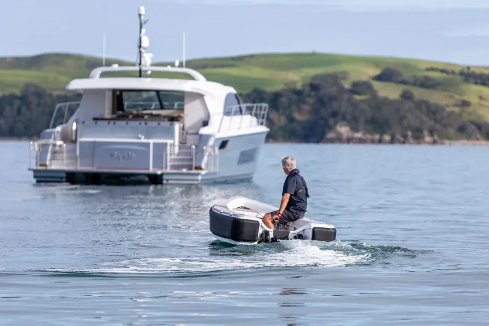 A man on top of a OCT powered by ZeroJet to a yacht some distance away green hills in background of water