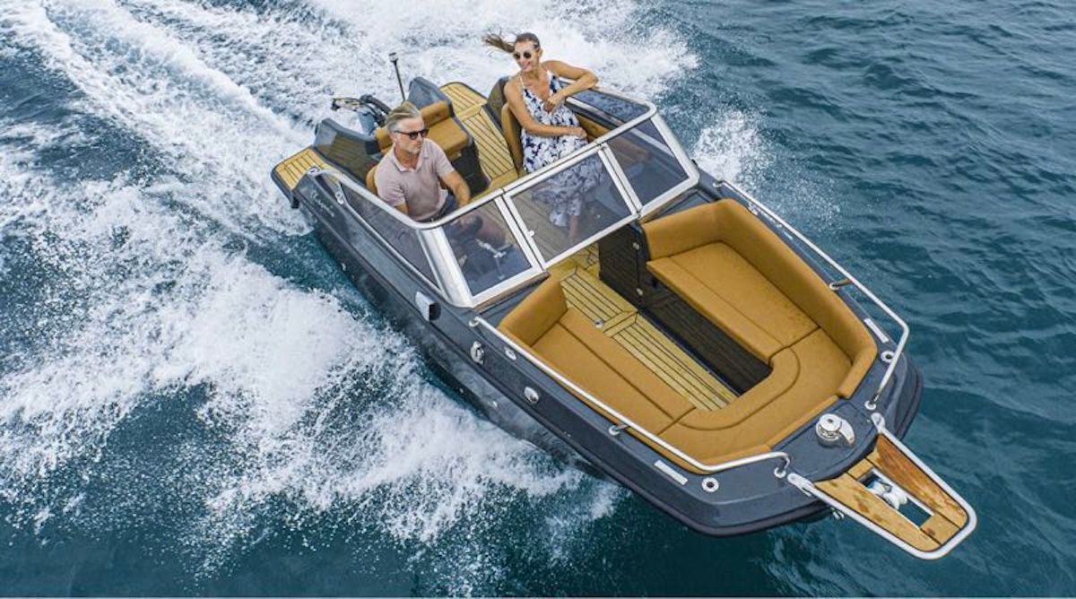 Above shot of two people in a bowrider boat with an open bow area for seating and brown interior, they are making a decent size wake behind the boat
