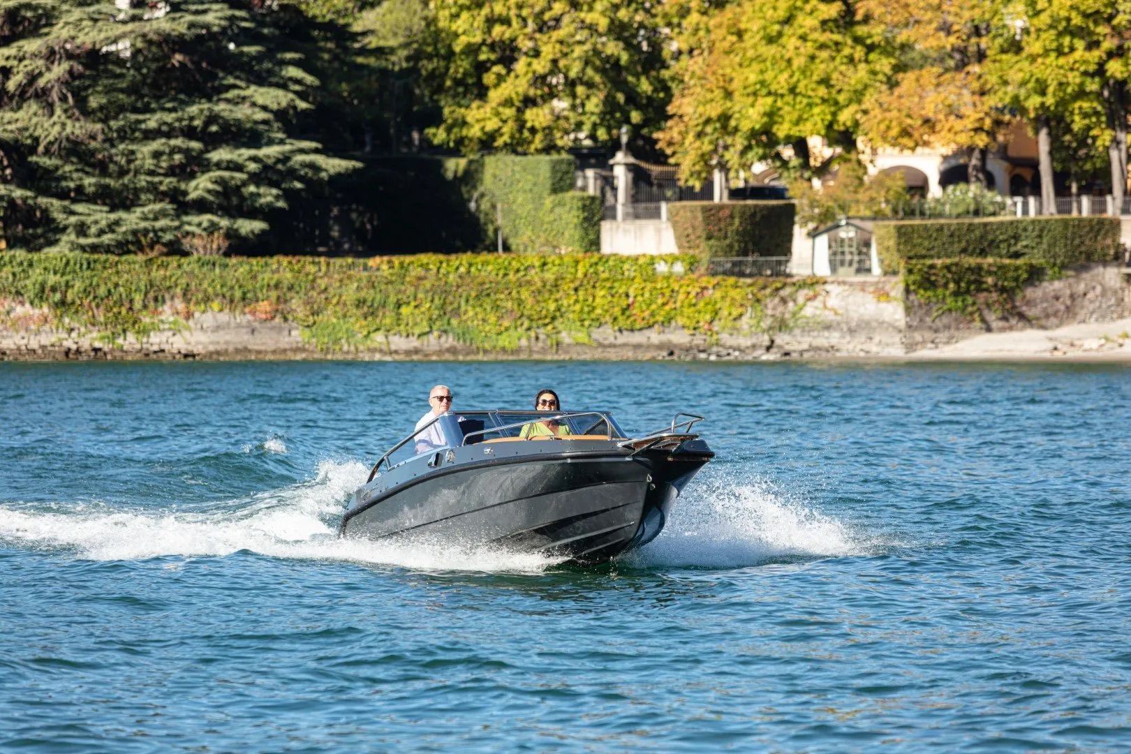 Black hull two people on boat going planning speeds on boat green foliage in background