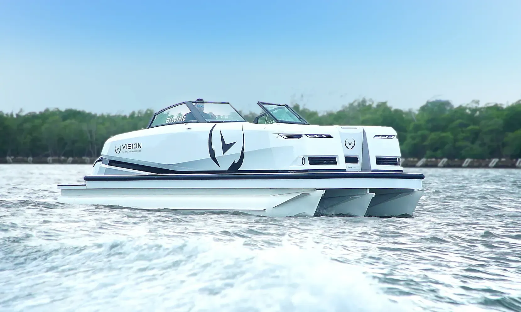 White hull tritoon boat sitting in water there is a man on the boat in the captain seat. The picture is taken at water level and clearly see the three hulls in the boat. There is a black V and semi circle around it on the side of the boat.