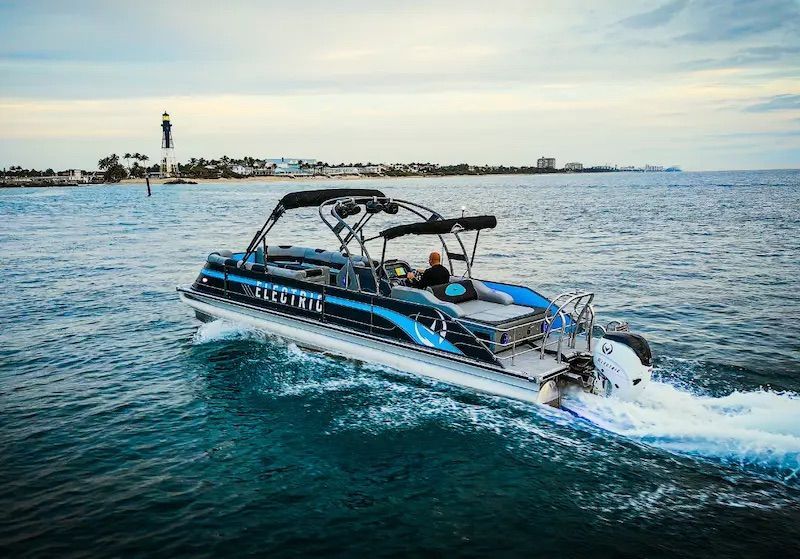 A black pontoon with blue accents is in water going planning speeds