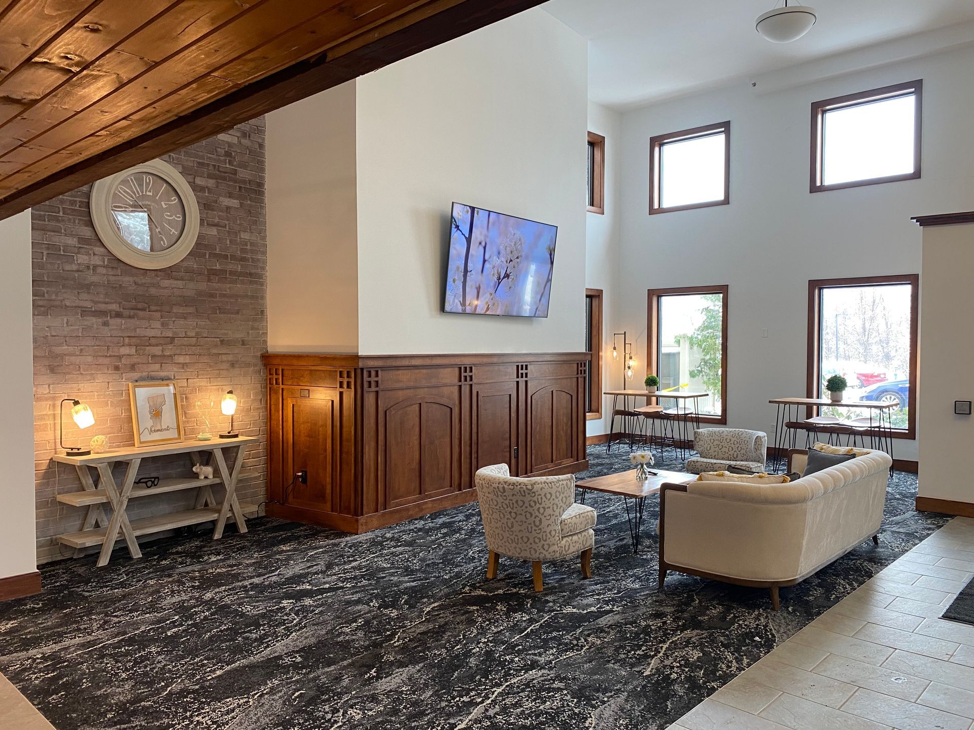 A living room with a couch , chairs , tables and a flat screen tv on the wall.