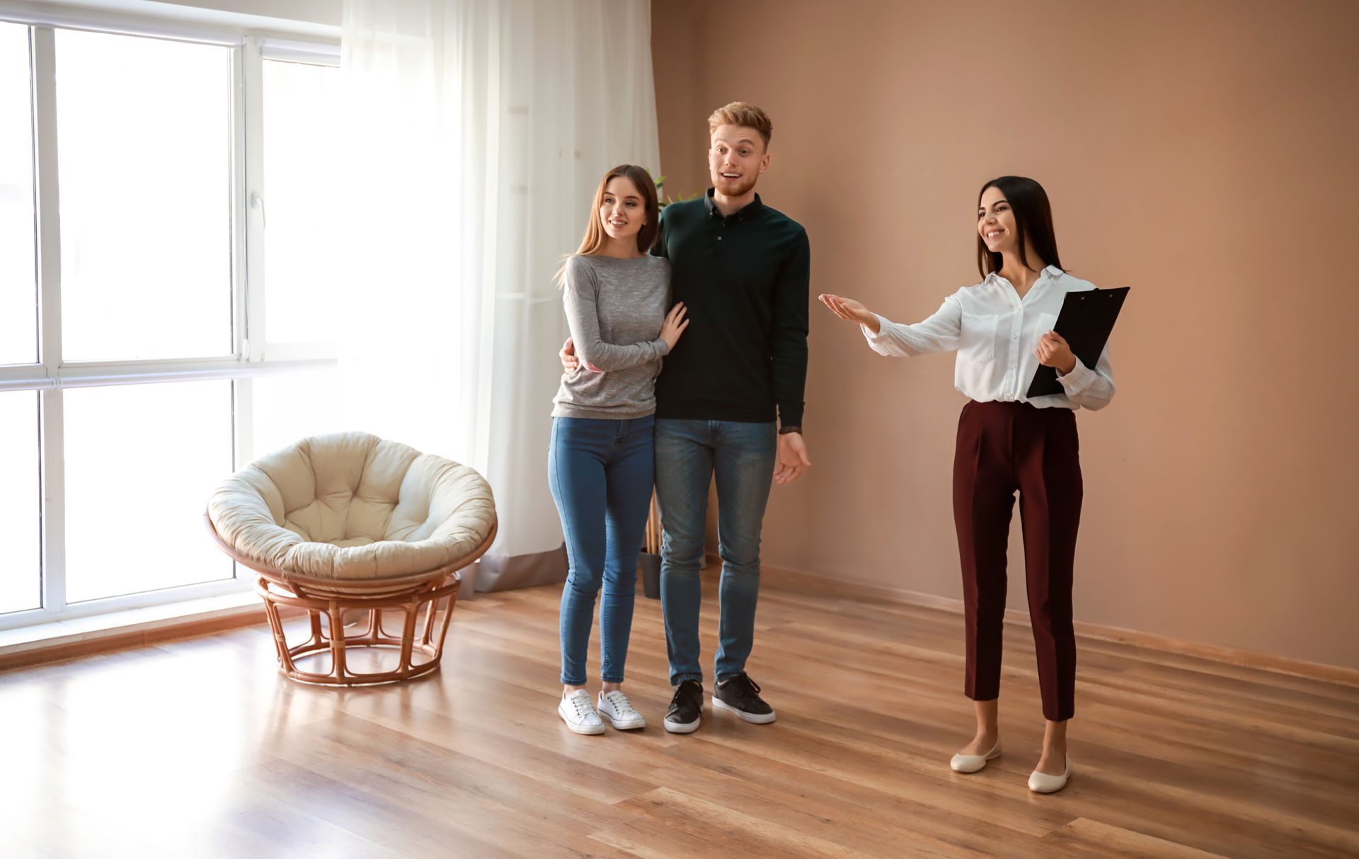 A man and a woman are standing in an empty room with a real estate agent.