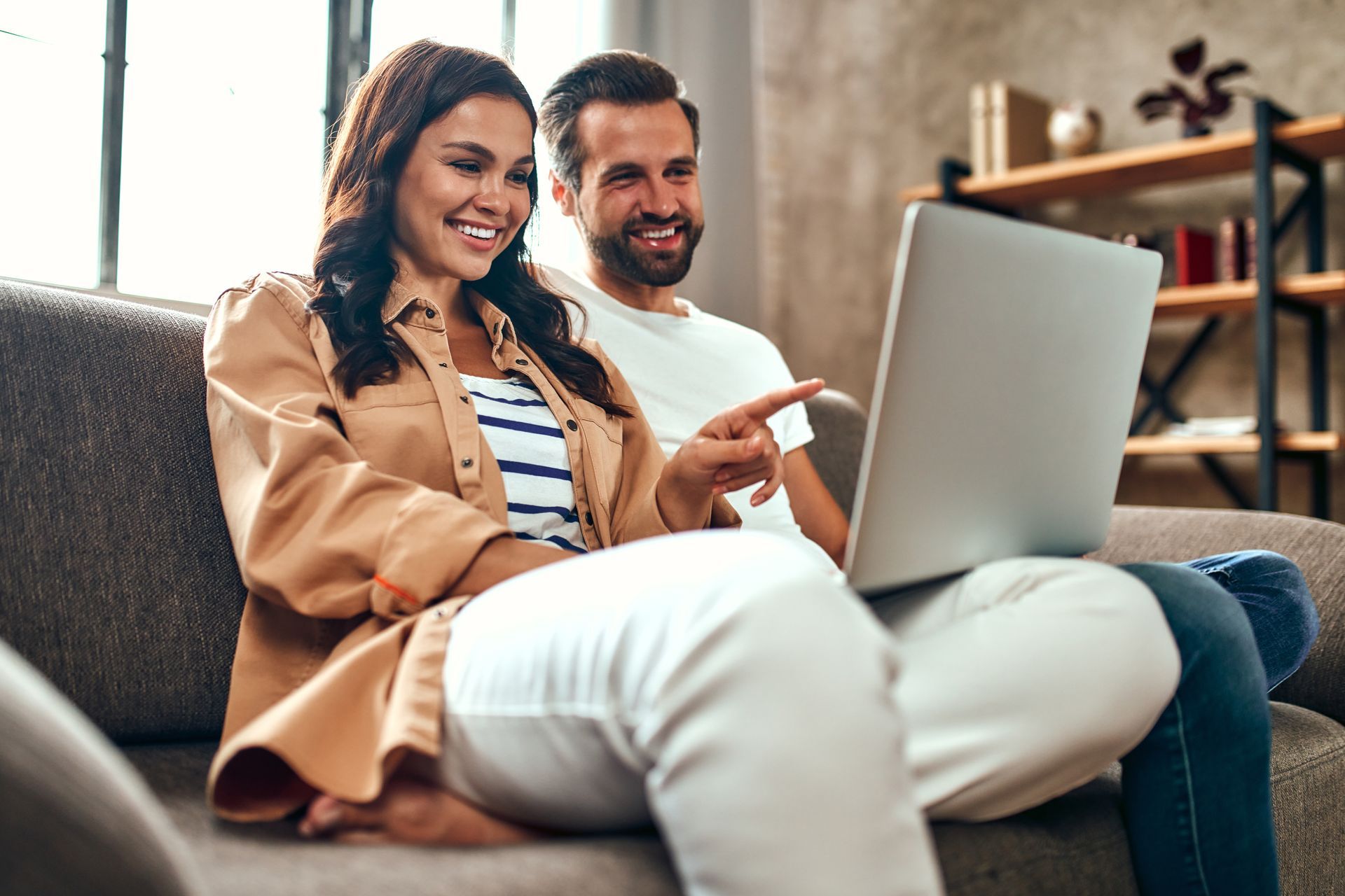 A man and a woman are sitting on a couch looking at a laptop.