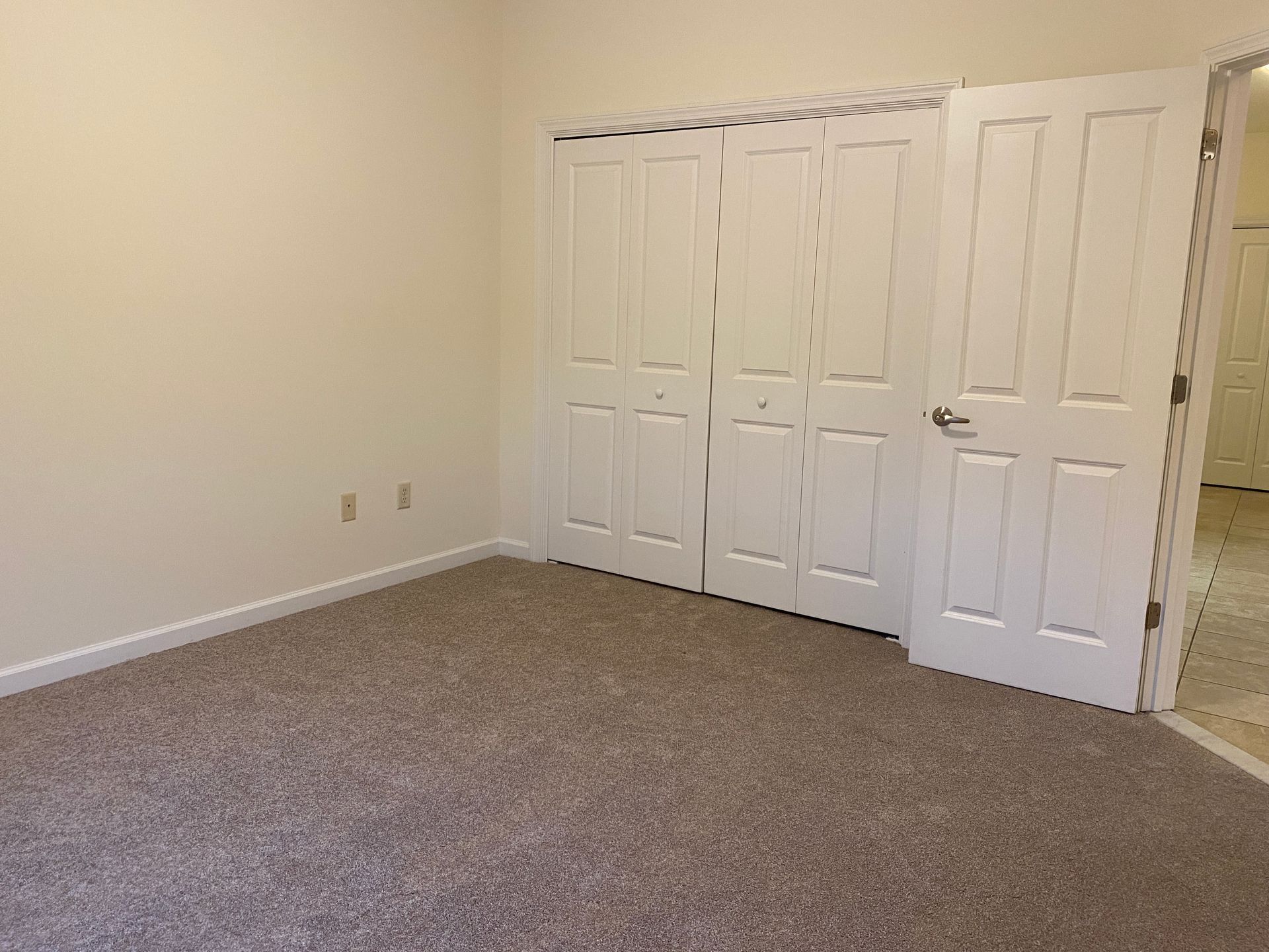 An empty bedroom with a carpeted floor and white closet doors.