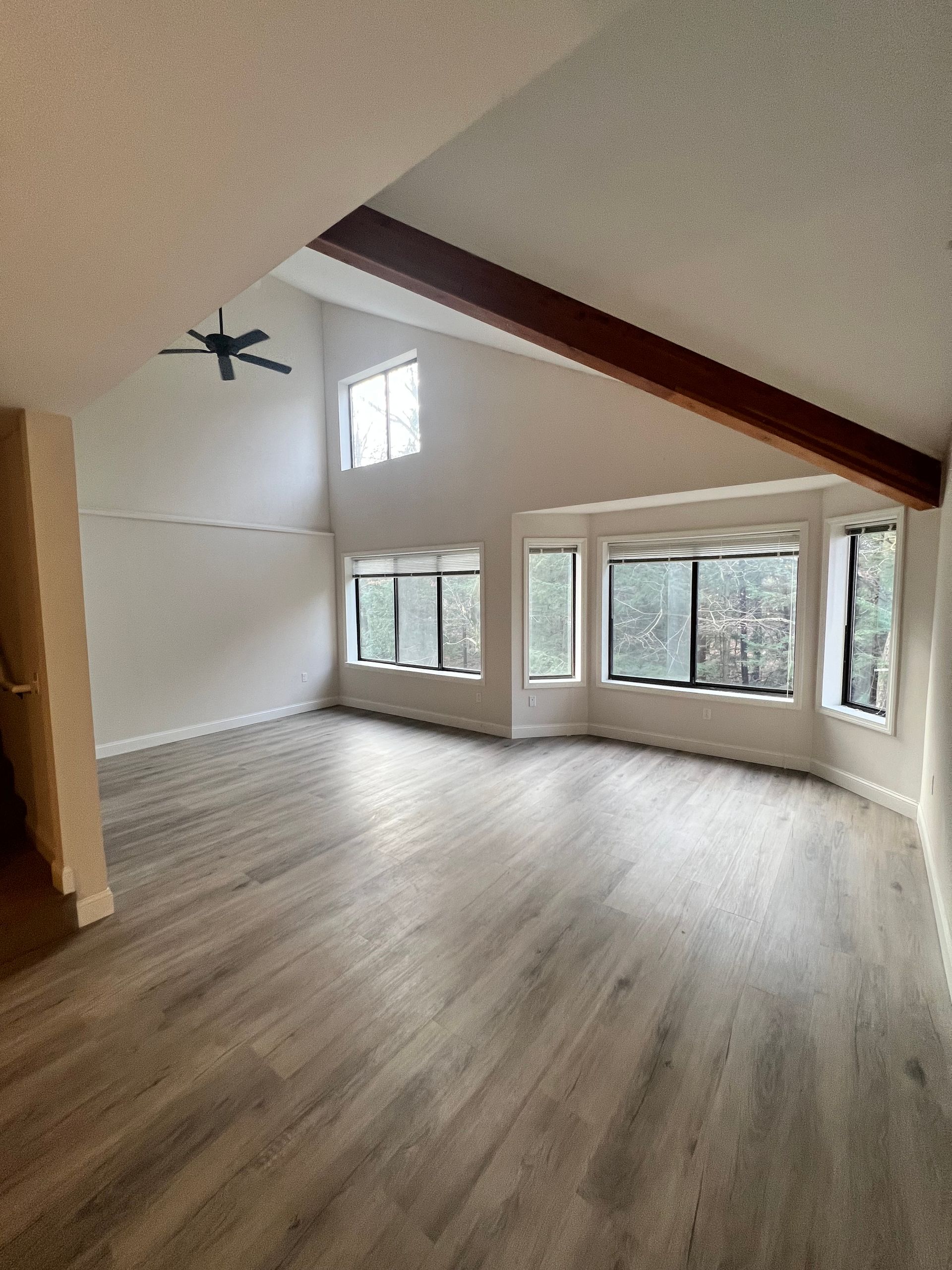 An empty living room with a ceiling fan and lots of windows.