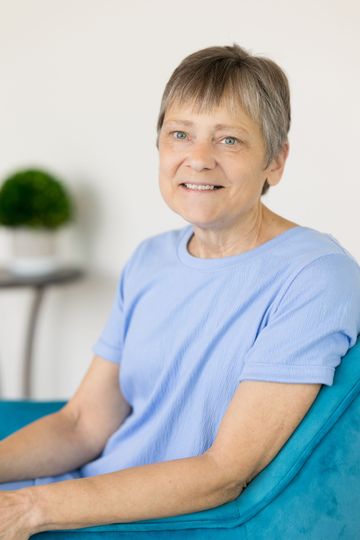 A woman in a white shirt is smiling in front of a window