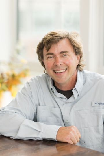 A man wearing a grey shirt with a black collar smiles for the camera