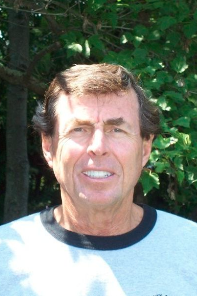 A woman in a blue and white shirt is smiling in front of a tree