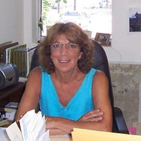 A woman in a blue shirt is sitting at a desk with her arms crossed.