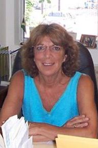 A woman in a blue shirt is sitting at a desk with her arms crossed.