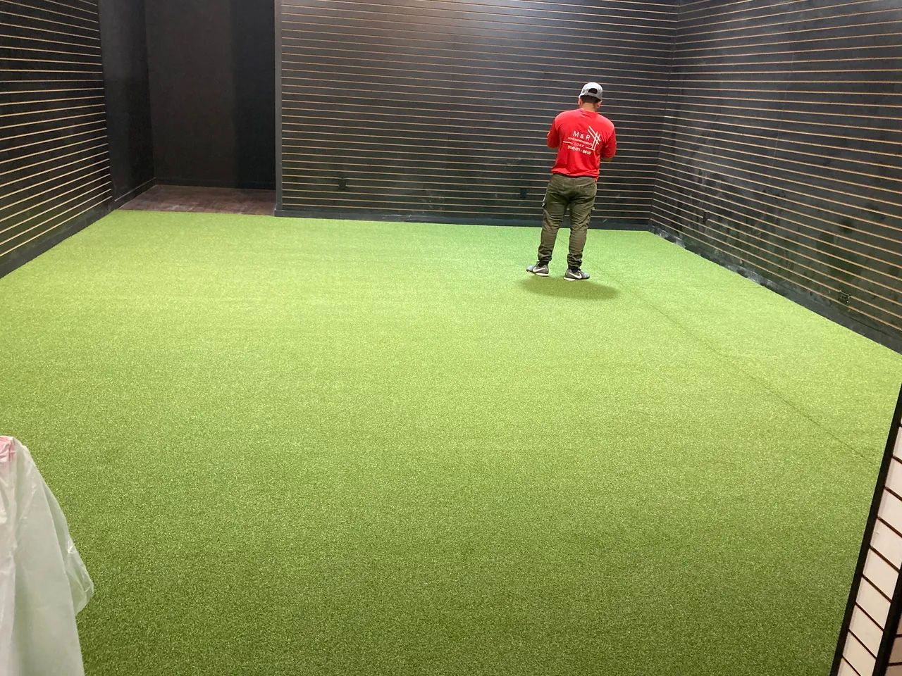 A man in a red shirt is standing in a room with a green carpet.