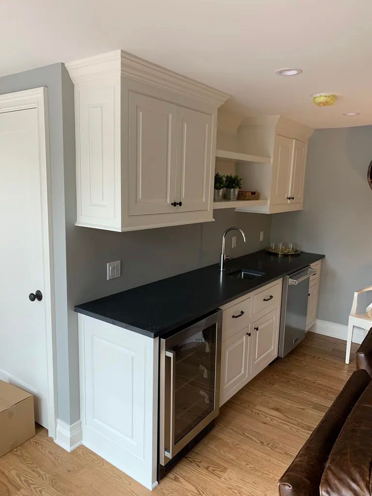 A kitchen with white cabinets , black counter tops , a sink and a refrigerator.