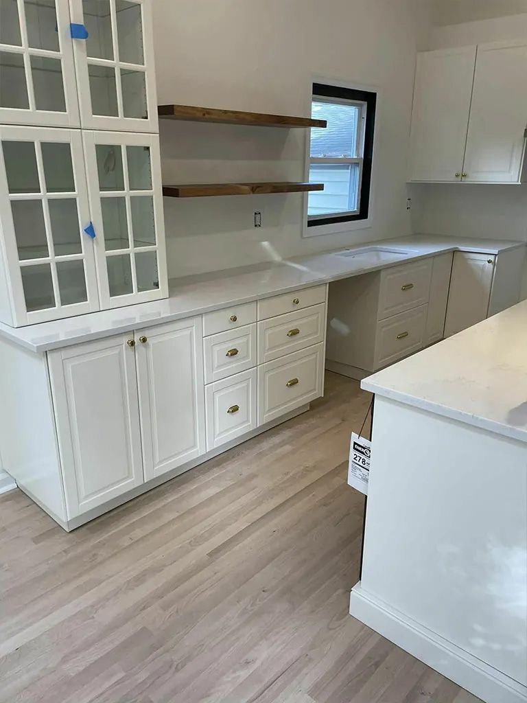 A kitchen with white cabinets , white counter tops , and wooden floors.