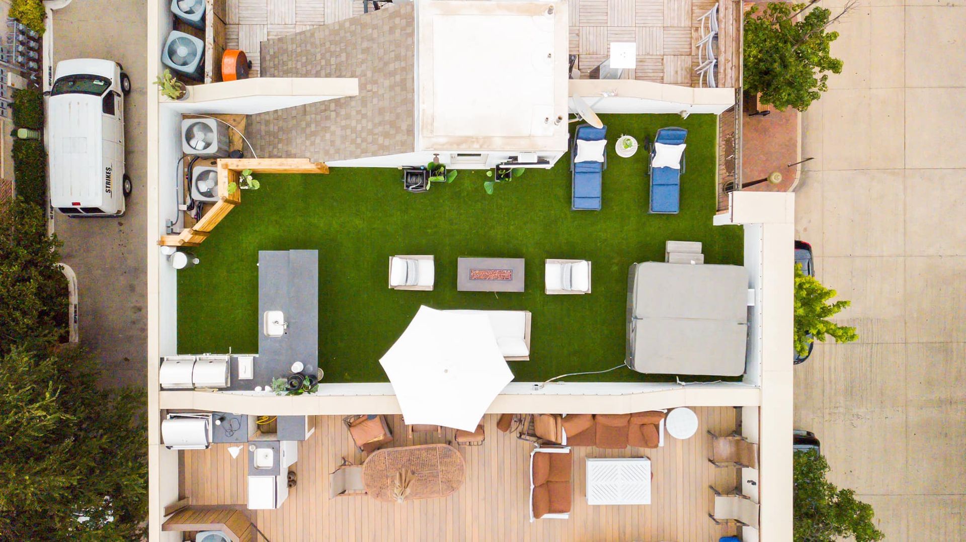 Overhead view of a rooftop with a van, artificial turf, seating areas, a hot tub, and an outdoor kitchen.