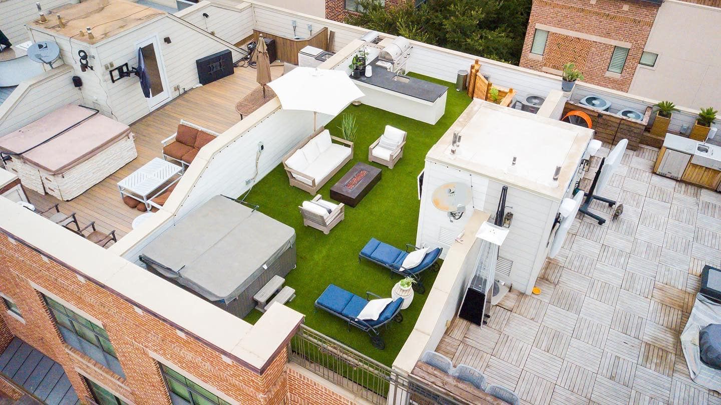 Rooftop patio with hot tubs, lounge chairs, green turf, a bar, and white walls.
