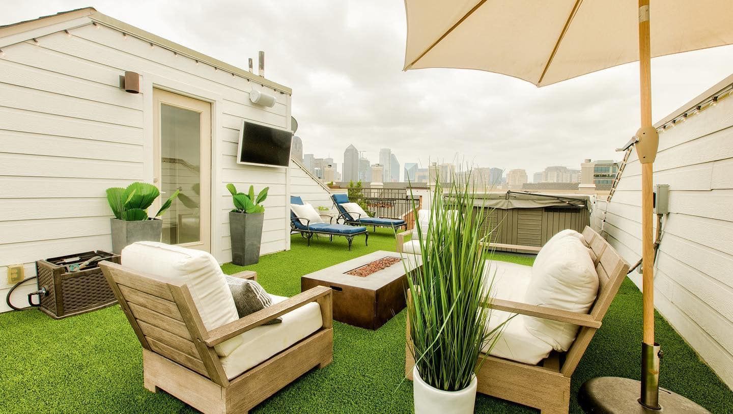Rooftop patio with wicker furniture, fire pit, umbrella, and a city skyline in the background.