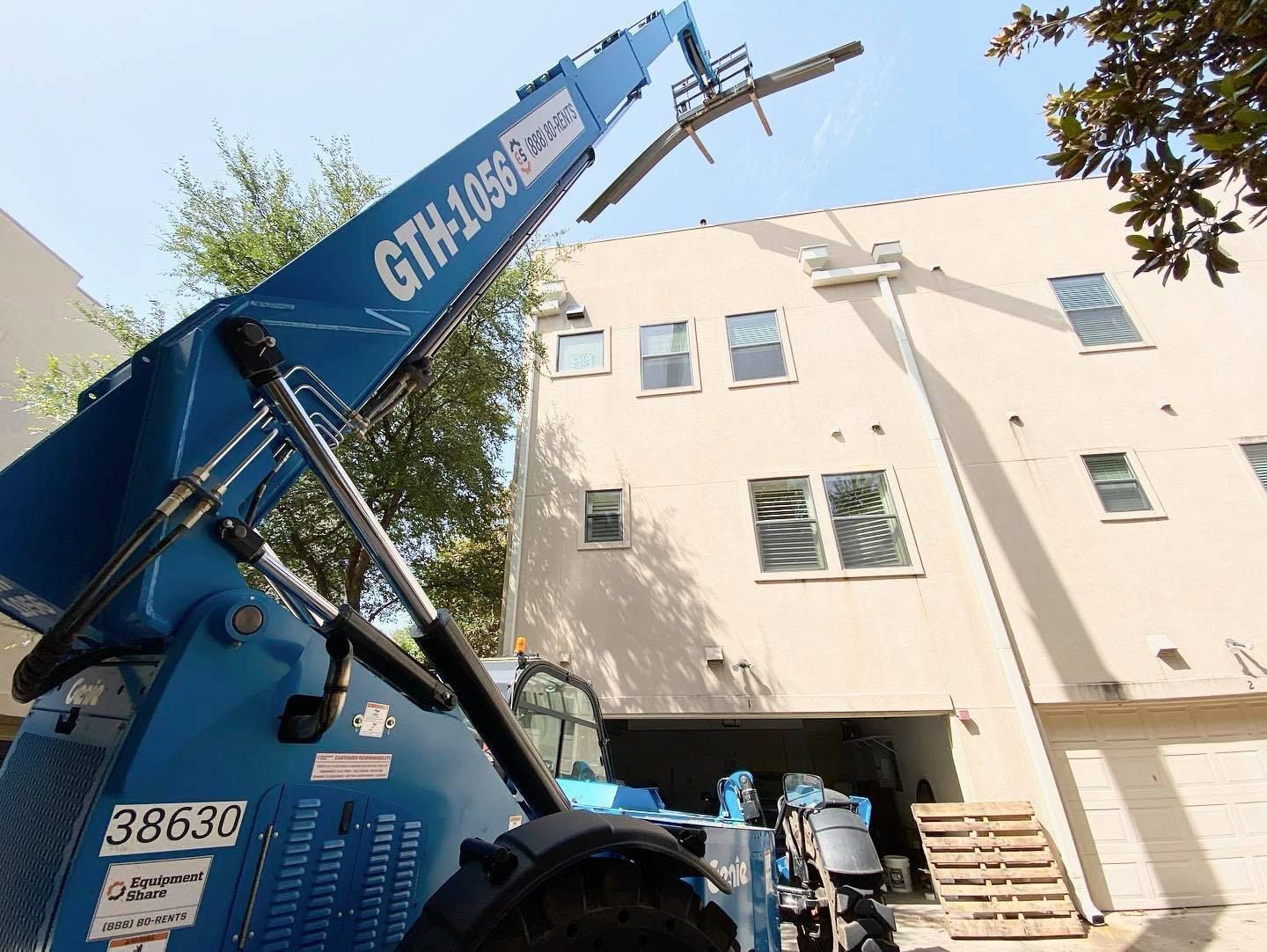 Blue telehandler lifting materials near a beige building.