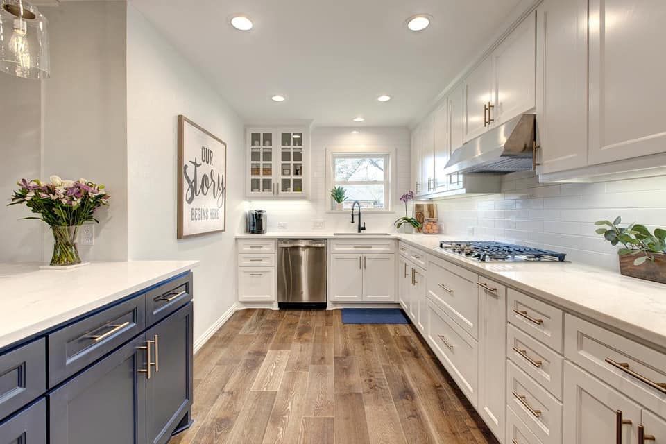 Modern kitchen with white and navy cabinets, stainless steel appliances, and wood flooring.