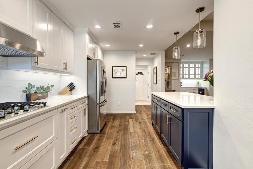 Modern kitchen with white and navy cabinets, stainless steel appliances, and wood flooring.