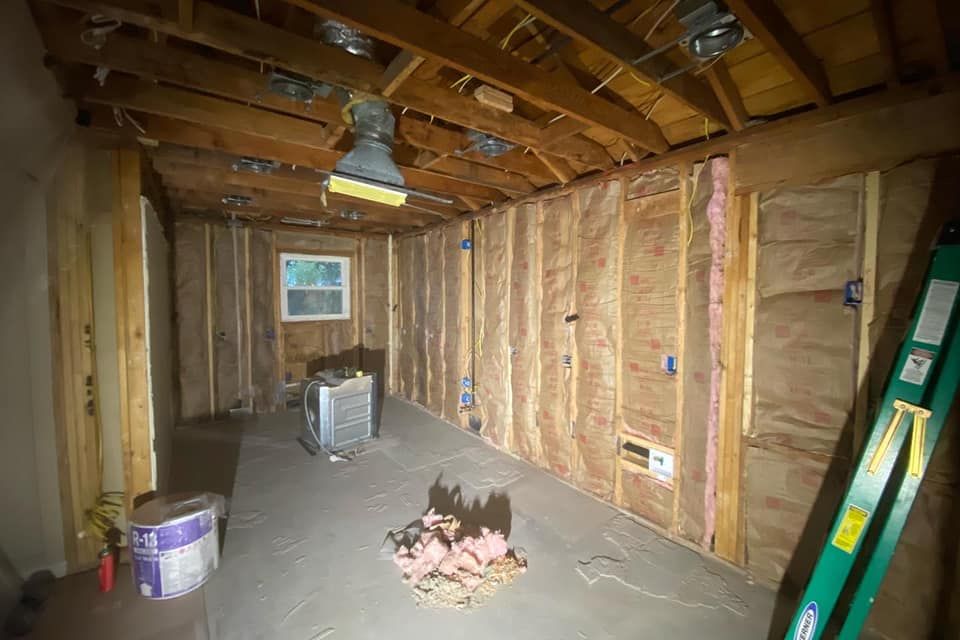 Interior of a room under construction with exposed wood framing, insulation, and a ladder.