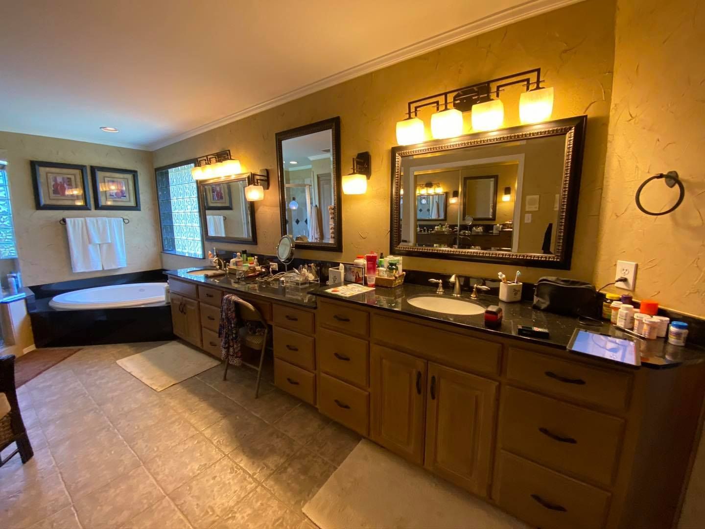 Spacious bathroom with dual sinks, mirrors, and a bathtub. Wooden cabinets and gold walls.