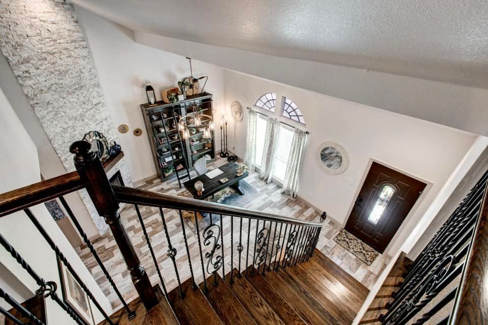 View from a staircase landing into a home office; wood and wrought iron details, high ceilings, large windows.