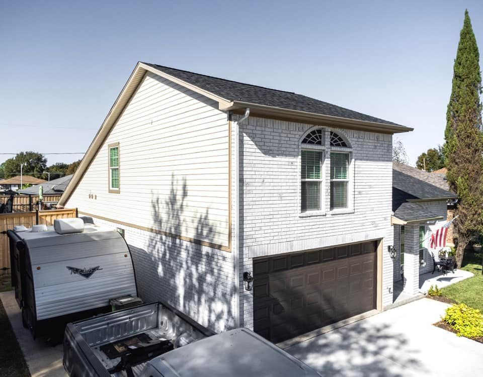 Two-story brick garage with a camper and truck parked in front; blue sky overhead.