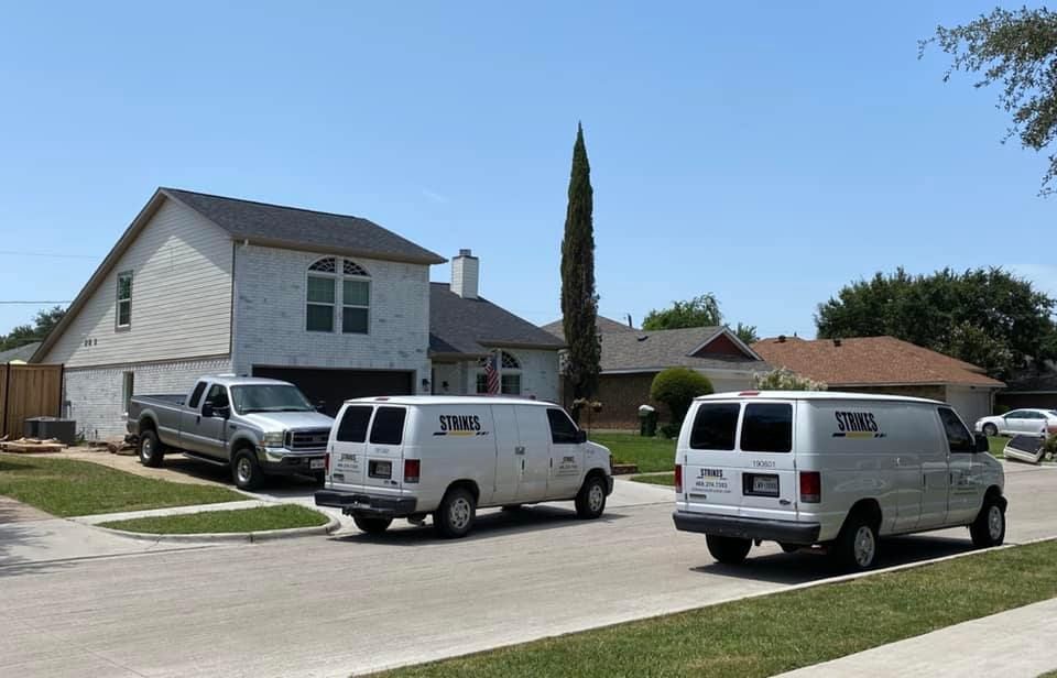 White service vans parked on a residential street. A two-story house is in the background. Sunny day.
