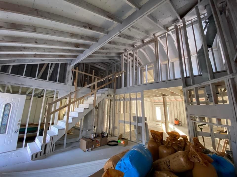 Interior of a building under construction, showing wooden framework, stairs, and a mezzanine level.